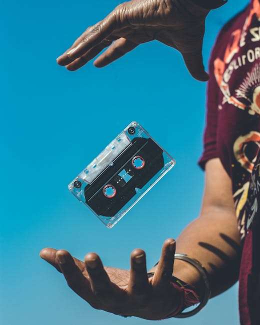 A retro cassette tape floating between hands against a clear blue sky, evoking nostalgia.